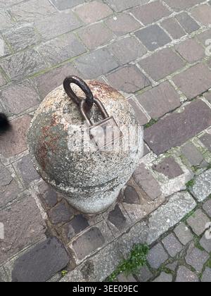 Vieux cadenas fermement attaché à un anneau métallique sur une borne en pierre texturée, représentant les concepts de sécurité, de restriction, de vieillissement et d'infrastructure urbaine Banque D'Images