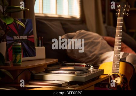 Gros plan du coin de la chambre affichant un lecteur de disque vinyle, guitare acoustique, cahier, boisson énergétique, affiche de musique rock, suggérer l'utilisation de la marque de loisirs et de style de vie créatif pour les jeunes Banque D'Images