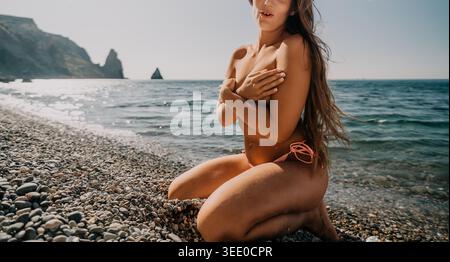Femme de plage agenouillée jeune dame posant sur le rivage de galets par la mer pour la détente de vacances d'été avec espace de copie Banque D'Images