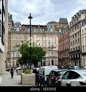 Paysage de rue historique de style européen avec façades en pierre ornées, voitures garées, piétons et ciel nuageux d'été dans un quartier du centre de Londres Banque D'Images