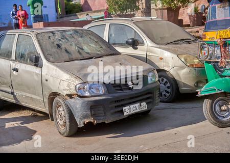 Une scène de rue dans le Rajasthan, en Inde, mettant en scène deux voitures à hayon poussiéreuses et usées garées au bord de la route. Au premier plan, une Suzuki Alto argentée avec Banque D'Images
