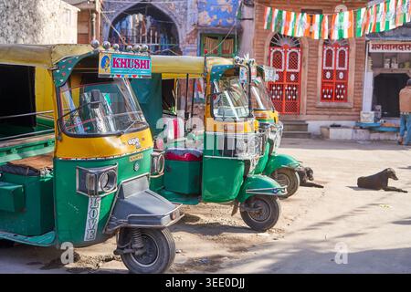 Trois auto-rickshaws (tuk-tuks) colorés peints dans les couleurs traditionnelles vert et jaune sont garés en rangée sur une rue poussiéreuse. Le véhicule le plus proche Banque D'Images