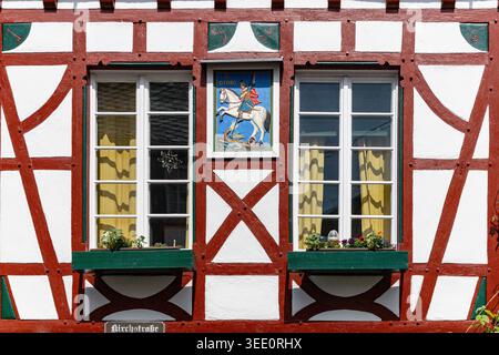 Vue sur une façade traditionnelle de maison à colombages représentant une icône de Saint George, une charpente en bois rouge et des fenêtres vertes à Monreal, Rhénanie-Palat Banque D'Images