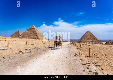 Vue d'ensemble du plateau de Gizeh avec les trois pyramides principales et une calèche typique tirée par des chevaux au centre. Banque D'Images