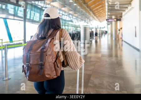 Femme voyageant à travers le terminal de l'aéroport avec sac à dos et bagages Banque D'Images