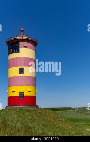 Vue sur le phare emblématique de Pilsum avec ses rayures jaunes et rouges distinctives debout sur une digue herbeuse sous un ciel bleu clair à Krummhorn, Nieder Banque D'Images