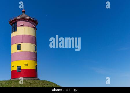 Vue sur le phare emblématique de Pilsum avec ses rayures rouges et jaunes distinctives debout sur un monticule herbeux sous un ciel bleu clair à Krummhorn, Niede Banque D'Images