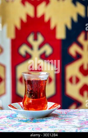 Verre armudu en forme de poire avec du thé noir sur une soucoupe décorée, avec un tapis traditionnel azerbaïdjanais en arrière-plan, Azerbaïdjan. Banque D'Images