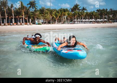 Heureux jeune couple partageant un moment joyeux sur des planches de surf lors de vacances tropicales Banque D'Images