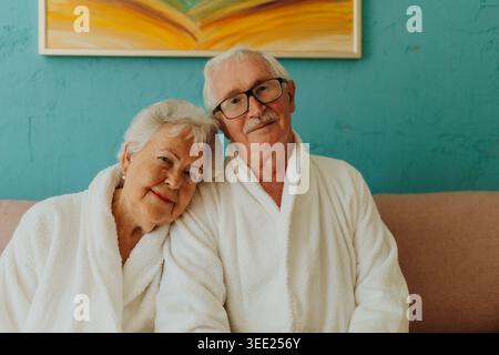 Portrait de couple senior heureux assis ensemble dans un peignoir sur un canapé. Banque D'Images