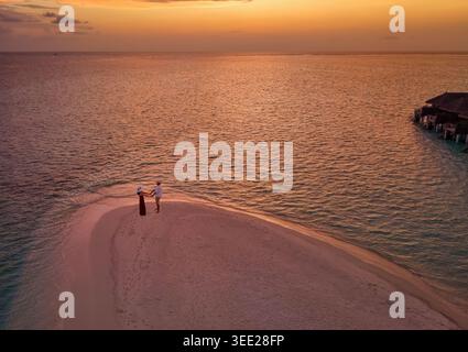 Vue aérienne élevée d'un couple de voyage romantique debout sur un banc de sable dans l'océan Indien pendant l'heure du coucher du soleil Banque D'Images