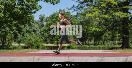 Jeune femme en sportswear noir courir sur une piste dans un parc Banque D'Images