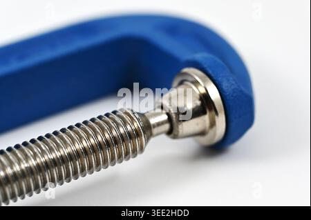 Macro gros plan d'une vis filetée en acier et d'un mécanisme de serrage en C bleu, mettant en évidence la texture métallique, l'ingénierie de précision et l'indust Banque D'Images