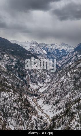 Vue d'une vallée enneigée profonde avec une rivière sinueuse et des pentes abruptes boisées de pins sous un ciel nuageux spectaculaire dans les montagnes Rocheuses CO, United S. Banque D'Images