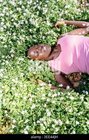 Femme paisible couchée dans les yeux du champ de fleurs blanches fermé souriant profitant de la vue de dessus du soleil de printemps Banque D'Images