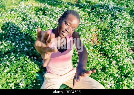 Black african american Joyful femme assise dans un champ de fleurs en fleurs avec un sourire amical Banque D'Images