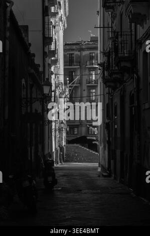 Photographie dramatique en noir et blanc d'une ruelle étroite à Catane, Sicile, Italie. La composition met en évidence le contraste frappant entre les Sun-dren Banque D'Images