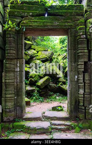 Une porte de grès frappante, finement sculptée et couverte de mousse verte vibrante, encadre un tas de pierres effondrées à l'intérieur d'un temple cambodgien, evoki Banque D'Images