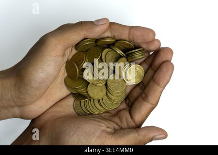 Une vue de haut en bas d'une paire de mains creusant une grande pile de pièces indonésiennes de couleur or. L'image symbolise l'épargne, la charité, la réussite financière, un Banque D'Images