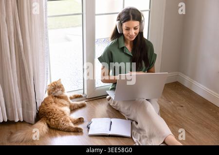 Femme travaillant sur ordinateur portable à la maison avec chat à proximité Banque D'Images