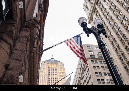 À Chicago, une vue du niveau de la rue montre de grands bâtiments et un drapeau américain suspendu à un lampadaire. Le ciel est dégagé. Les gens vont à peu près leur jour être Banque D'Images