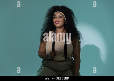 Femme afro-américaine dans les années 30 assise dans un studio sarcelle portant un bandeau beige bretelles noires Banque D'Images