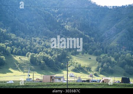 Vue panoramique d'un paysage rural avec des structures en bois et des collines verdoyantes sous un ciel bleu clair dans une région montagneuse Banque D'Images
