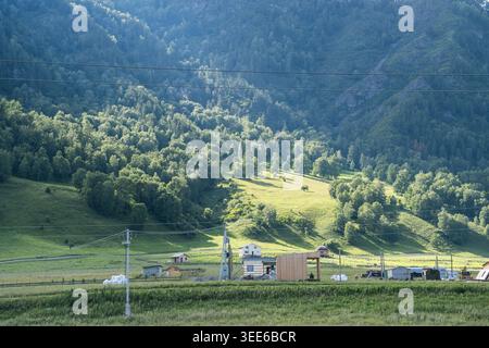 Vue panoramique sur les collines verdoyantes et les bâtiments ruraux sous un ciel clair dans une région montagneuse avec des arbres et des champs au premier plan Banque D'Images