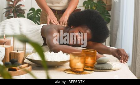 Femme souriante recevant un massage du dos au spa relaxant avec des bougies et des pierres chaudes Banque D'Images