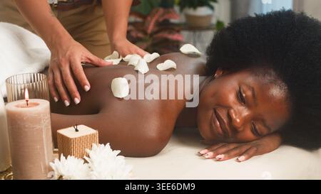Massage spa relaxant avec pétales de rose sur femme souriante couchée sur la table de massage Banque D'Images