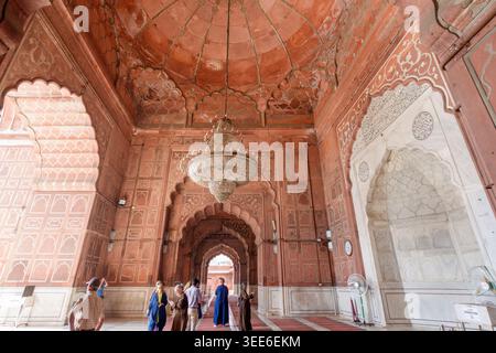 Intérieur de la grande mosquée Jama Masjid à Delhi Inde avec des arches de grès rouge et un grand lustre central avec les visiteurs dans la salle de prière Banque D'Images