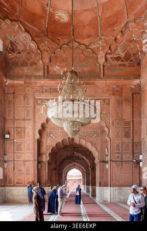 Intérieur de la grande mosquée Jama Masjid à Delhi Inde avec des arches de grès rouge et un grand lustre central avec les visiteurs dans la salle de prière Banque D'Images