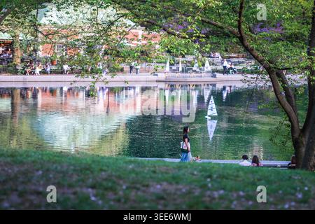 Vue sur Central Park Conservatory Water avec un voilier modèle sur l'étang, les gens marchant le long du chemin, et les arbres verdoyants au printemps New York, New York Banque D'Images