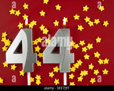 Concept de célébrer l'anniversaire et l'anniversaire. Numéro 44 quarante-quatre bougie d'anniversaire de célébration en argent sur fond rouge festif. Quarante-quatre ans b Banque D'Images