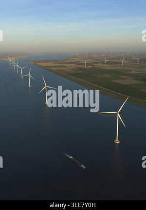 Vue aérienne des éoliennes dans une rangée dans l'eau à côté d'un canal avec une barge cargo et des champs verts au coucher du soleil pays-Bas. Banque D'Images