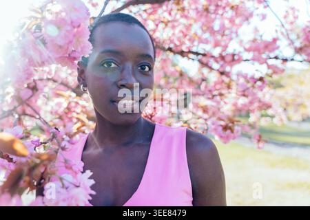 Gros plan portrait de femme heureuse avec fleur de cerisier rose dans le parc de printemps ensoleillé Banque D'Images