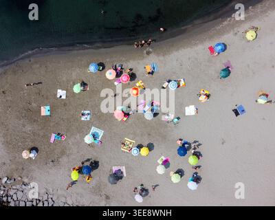 Vue aérienne de parasols colorés et de serviettes dispersés sur le sable avec des personnes bronzant près de l'eau de mer sombre à San Lorenzo, Ligurie, Italie Banque D'Images