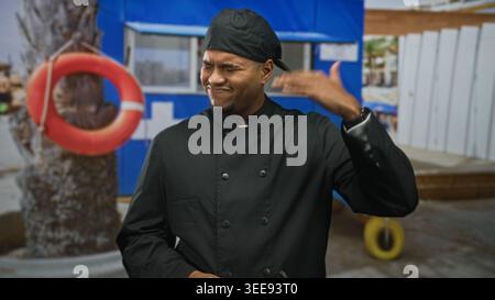 Homme chef en uniforme noir tenant le coucou, geste de la main à la tête à côté de lifering et palmier à un kiosque de plage côté rue ; frustration. Banque D'Images