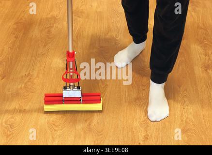 Personne portant des chaussettes blanches debout à côté d'une serpillière sur un plancher de bois propre, effectuant les tâches ménagères et l'entretien Banque D'Images
