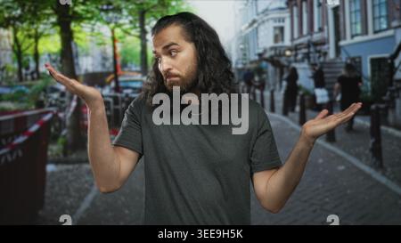 L'homme haussa les paumes au milieu de la rue de la ville avec les épaules levées et les avant-bras visibles ; dilemme de l'incertitude et de l'indécision. Banque D'Images