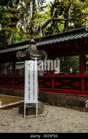 Lanterne en pierre avec panneau japonais devant la clôture rouge du sanctuaire en bois et le toit en tuiles du sanctuaire Nezu, quartier Bunkyō, Tokyo, Japon Banque D'Images