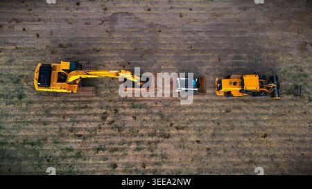 Vue aérienne d’engins de chantier lourds, y compris une excavatrice, une chargeuse stationnée en rangée sur un champ agricole labouré à Loma, Banque D'Images