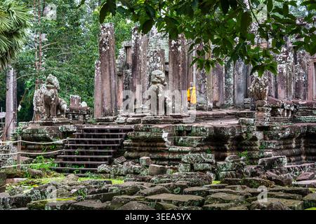 Vue imprenable sur le temple du Bayon avec d'anciennes statues de gardien de lion en pierre et un moine vêtu de robes orange parmi les colonnes. La scène capture le mystique Banque D'Images
