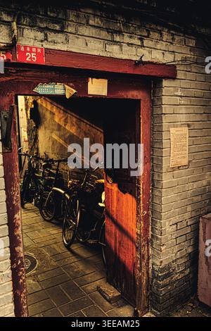 Porte en bois rouge vintage à No.25 Lianfeng Hutong, Pékin, Chine. La lumière dorée chaude de l'après-midi coule à travers la porte ouverte, projetant une longue ombre Banque D'Images