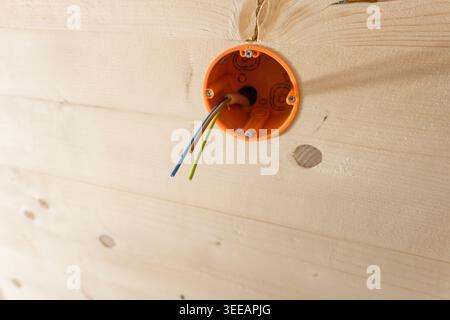 Câble électrique à trois fils sorti de la prise murale orange. Gros plan sur la technologie du logement. Installation électrique dans une pièce domestique en Allemagne. Banque D'Images