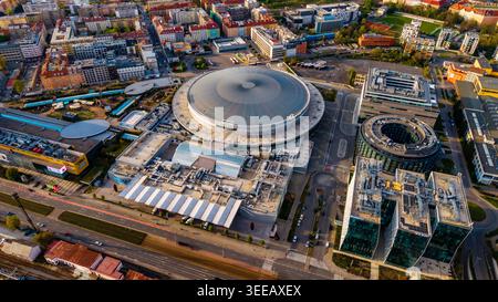 Cheskomoravska, Tchéquie - 21 avril 2026 : vue aérienne de O2 Arena entourée d'immeubles de bureaux modernes et de blocs résidentiels sous la lumière du soleil. Banque D'Images
