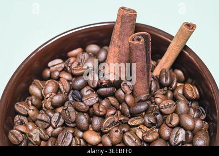 Grains de café torréfiés avec des bâtonnets de cannelle, anis étoilé dans une tasse en céramique brune sur fond bleu demi vue macro Banque D'Images