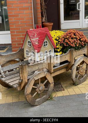 Chariot en bois rustique avec maison miniature décorative et fleurs d'automne dans une rue confortable Banque D'Images