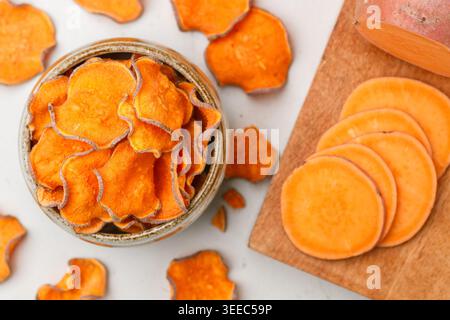 Croustilles douces biologiques saines dans un bol et patates douces fraîches sur une planche de bois. Apéritif végétarien et végétalien. Régime alimentaire. Une collation utile. Selecti Banque D'Images