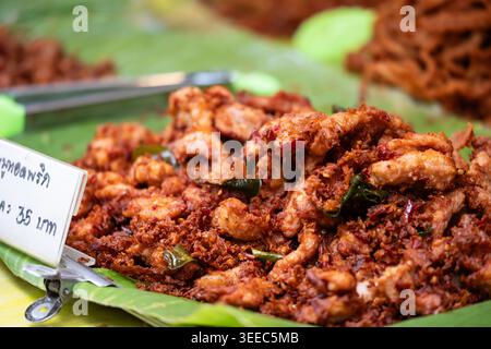Porc épicé frit avec piments séchés et feuilles de citron vert kaffir croustillantes servies sur une feuille de banane dans un marché thaïlandais de Street food. Banque D'Images